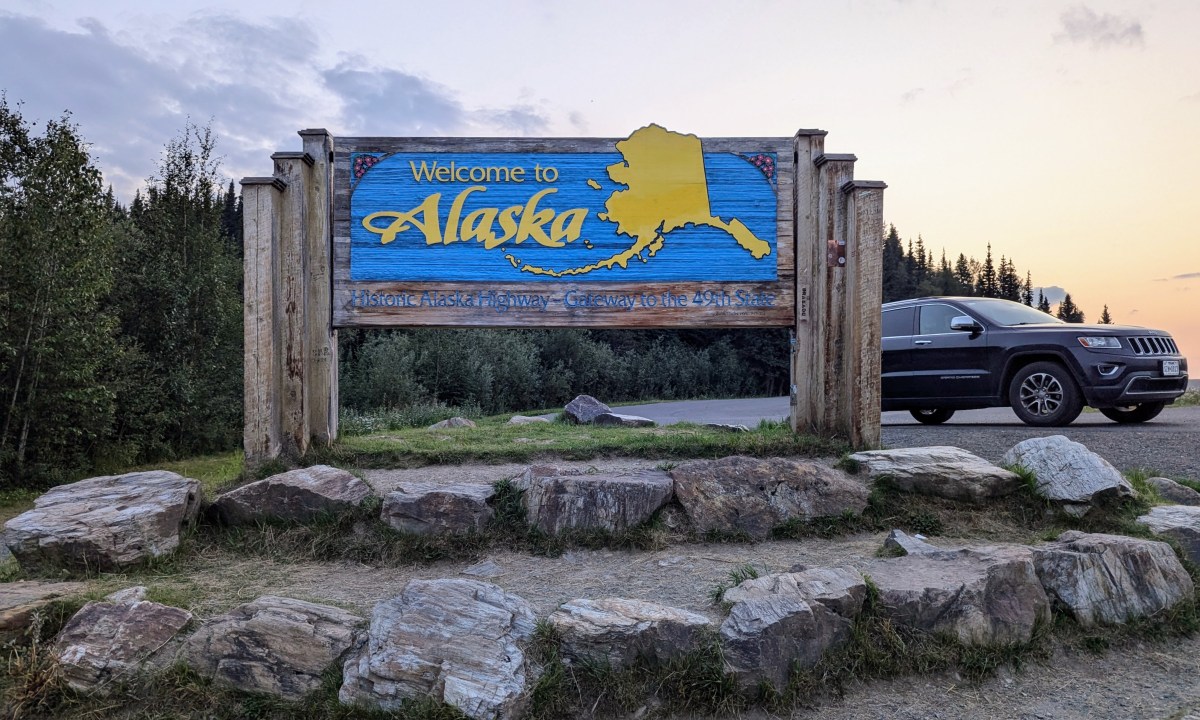 The state sign for alaska with a car behind it