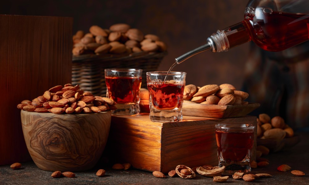 Italian liqueur Amaretto with almonds nuts on a vintage table. Liqueur is poured from a bottle into a glass.