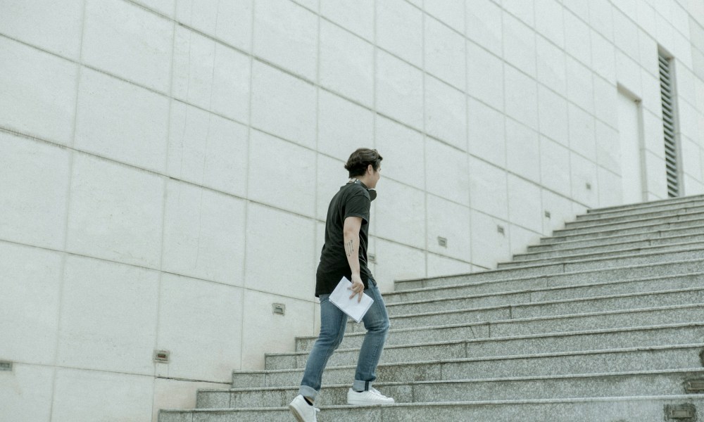 Man walking up stairs wearing jeans and white sneakers outside concrete