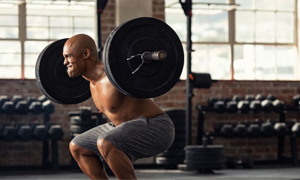 man doing a squat with barbell grey shorts