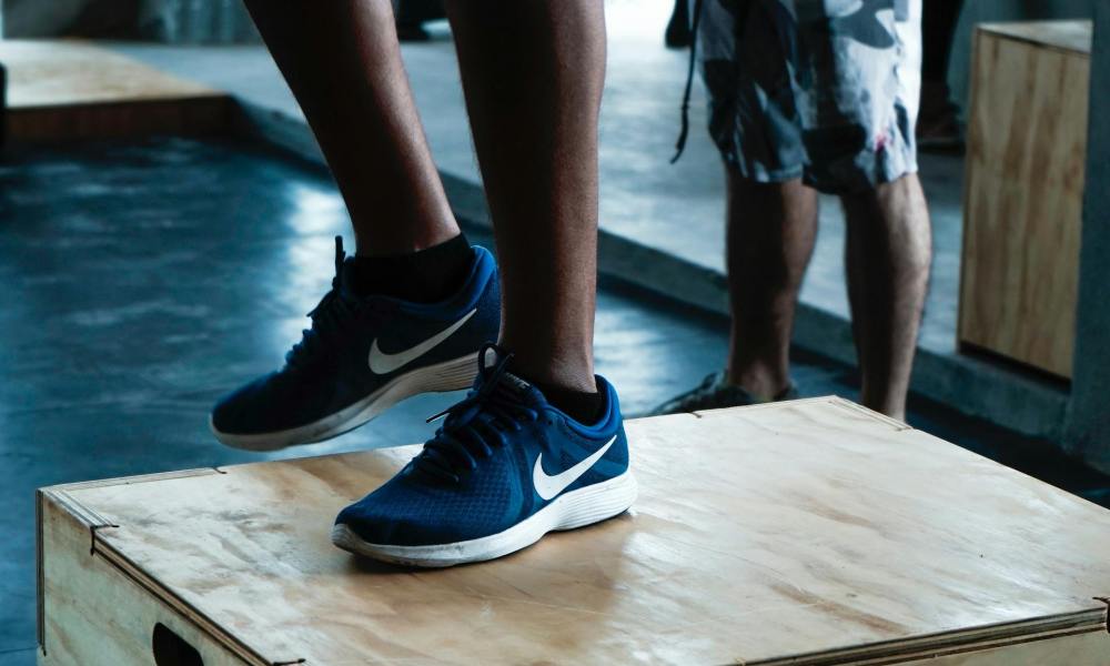 Close-up man legs wearing blue sneakers doing step-up exercise in gym