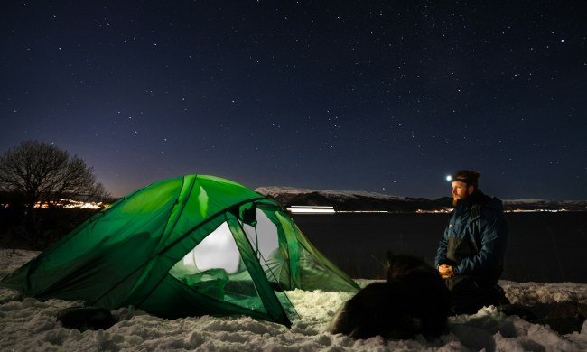 Man winter camping with a green tent