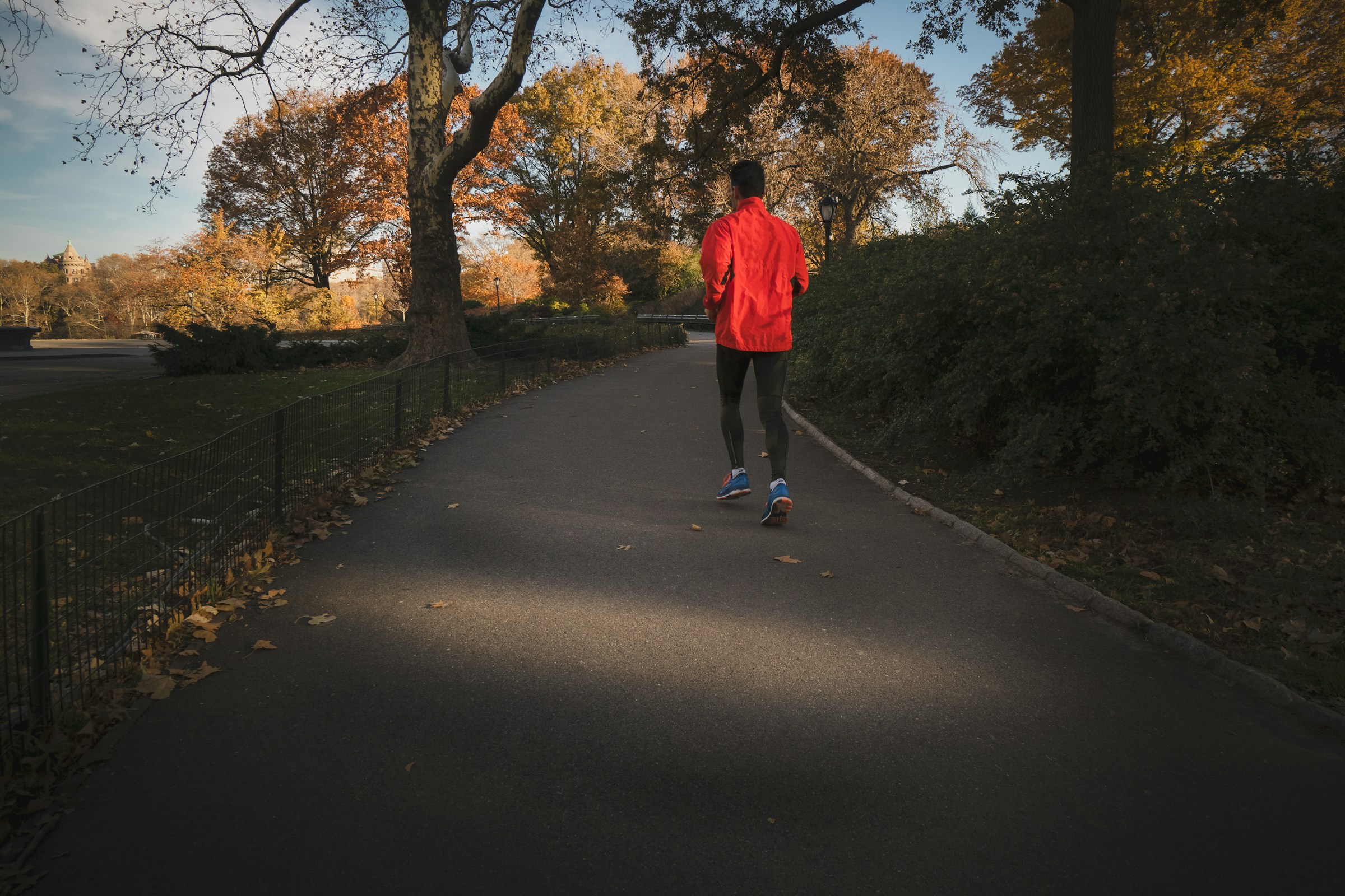 homme courant à travers les arbres sur le chemin portant une veste rouge