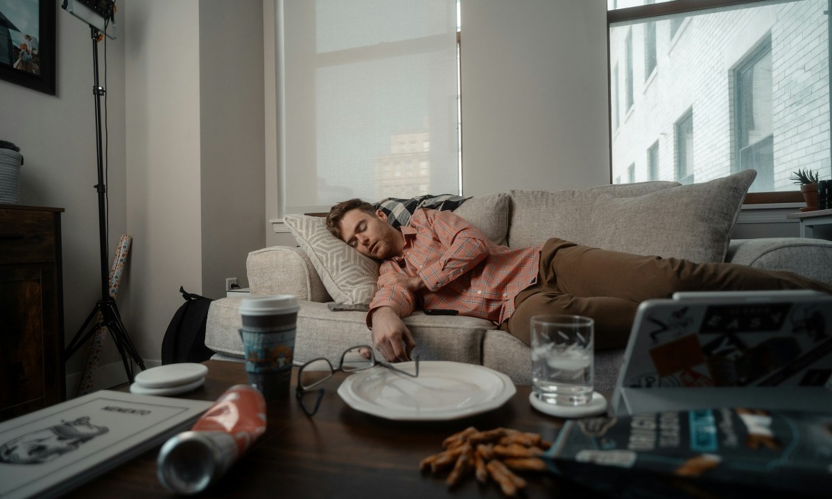 man laying on couch sleeping with messy table empty food plates glasses