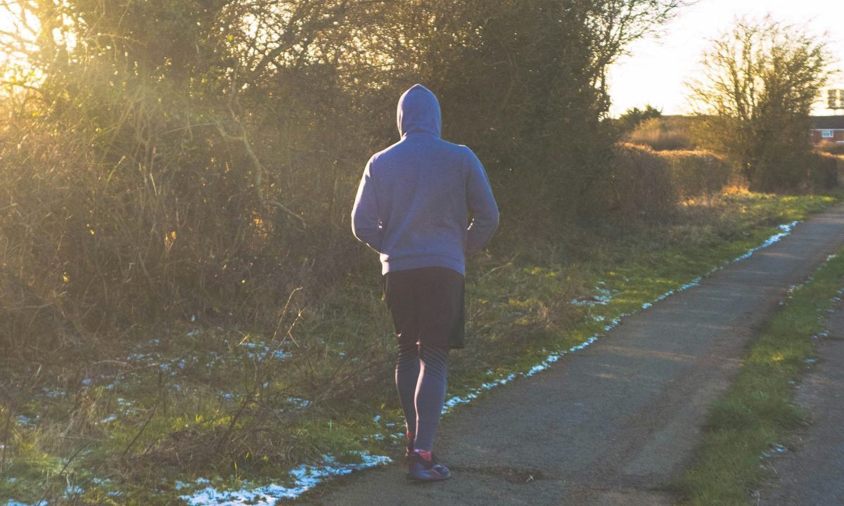 man running outside wearing hoodie sun shining through trees