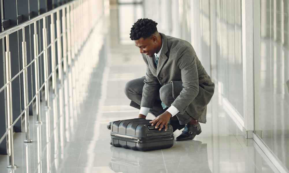 man in suit sitting on the ground in airport looking at suitcase