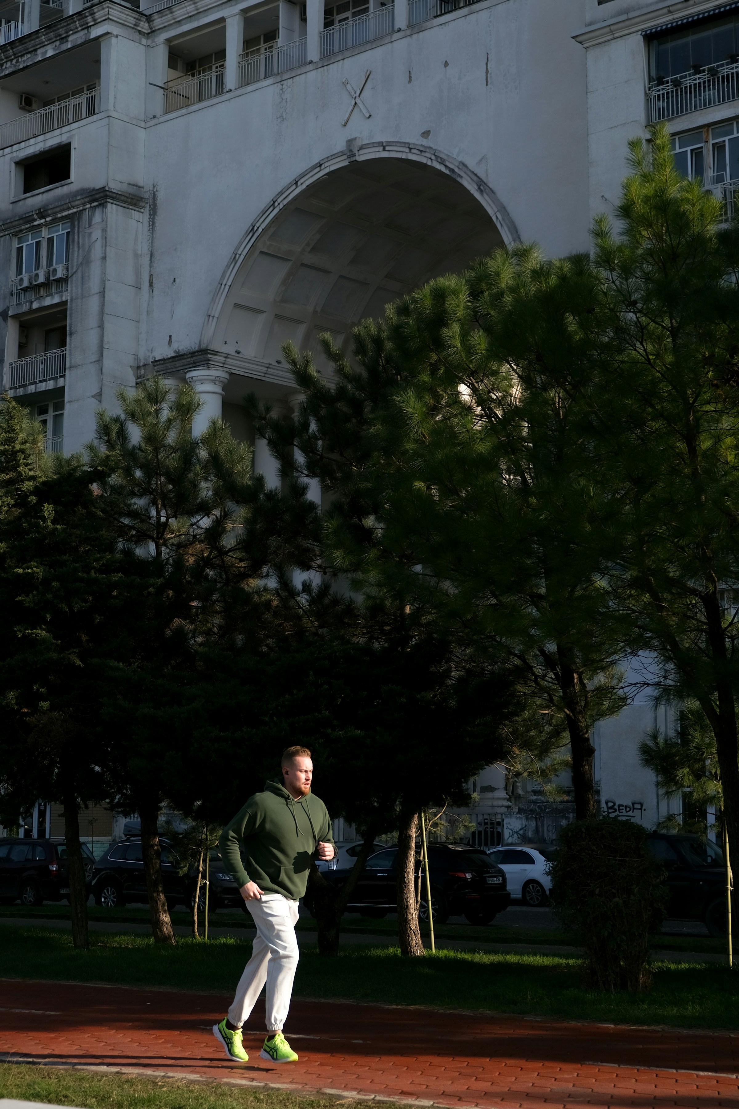 homme en sweat à capuche vert courant près du bâtiment et des arbres