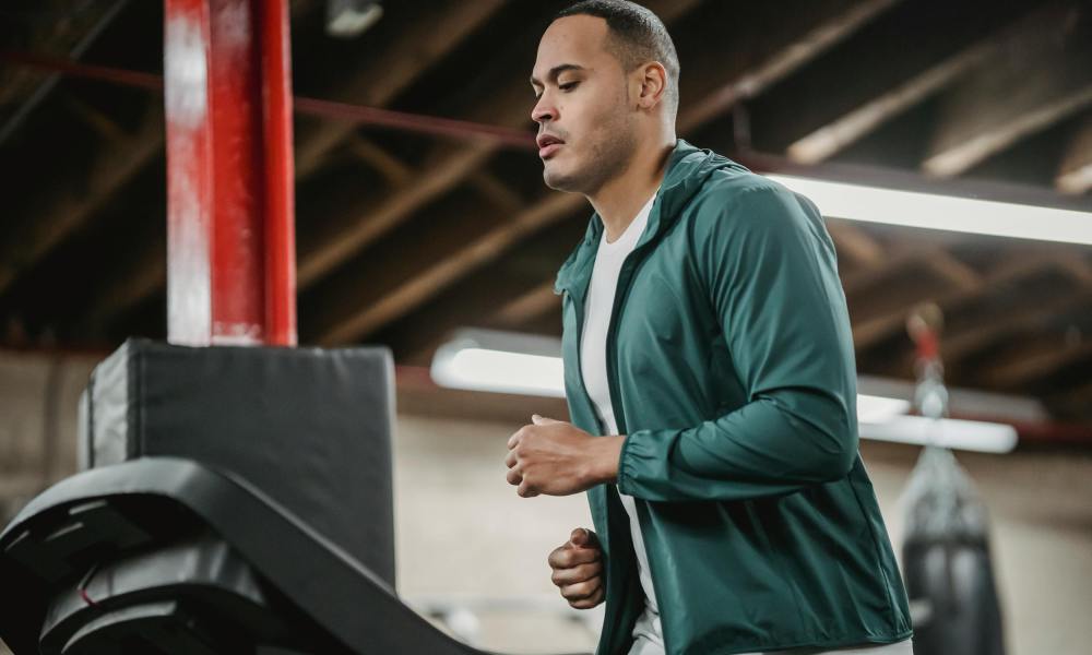 Man running on treadmill wearing blue jacket in gym