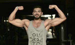 Man flexing arms muscles on a dark background in the gym