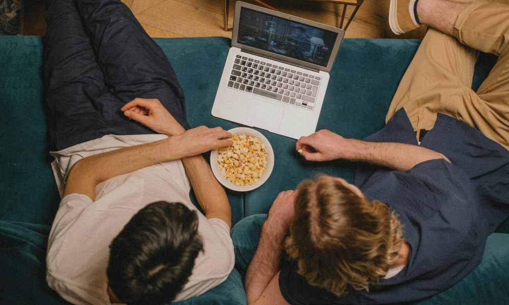 Men eating popcorn while woman is on a laptop