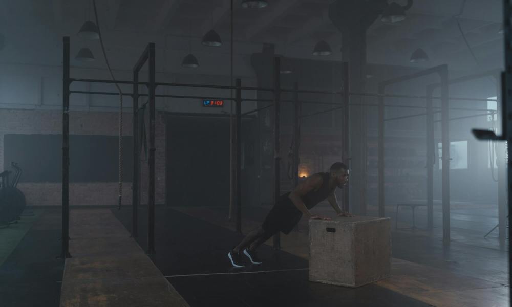 man doing incline push up in gym on wooden plyo box dark room