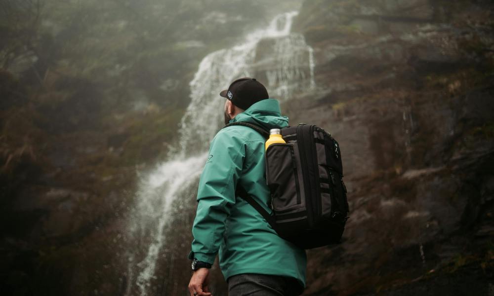 Man wearing green and hat rucking backpack rucksack walking in nature by waterfall with drink water