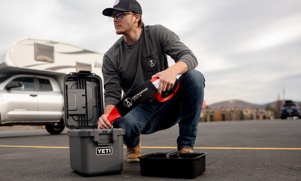 Man next to a truck camper opening the Uncharted Supply Co. X Yeti Overlander emergency kit.