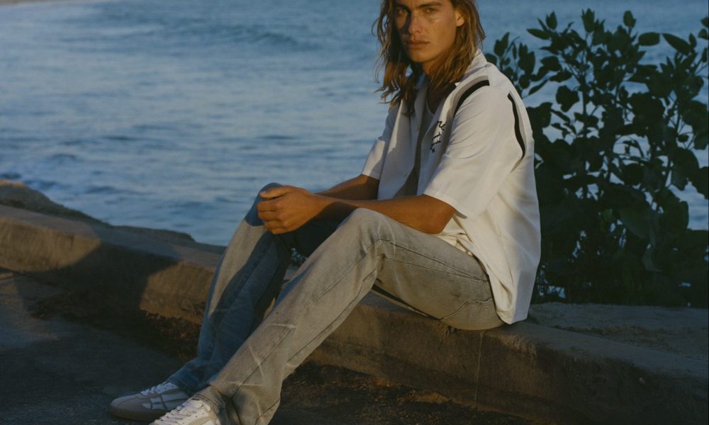 man sitting next to edge wearing white leather sneakers