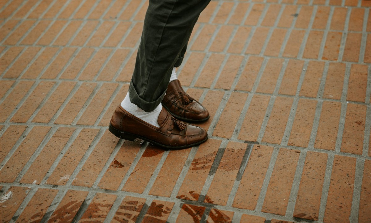 Person wearing brown leather shoes on bricks