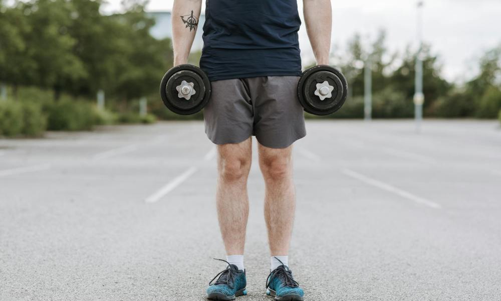 man doing dumbbell shrug holding dumbbells outside standing in parking lot