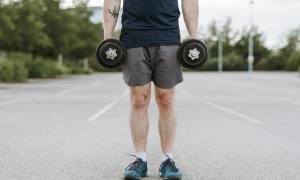 man doing dumbbell shrug holding dumbbells outside standing in parking lot