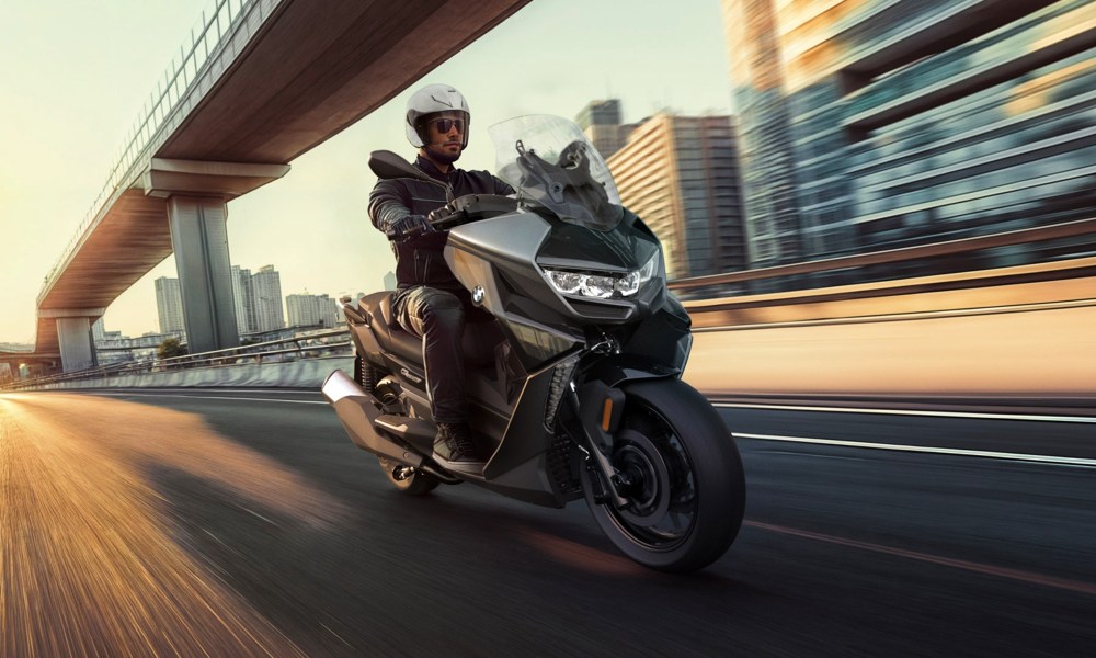 Single rider on a 20254 BMW C 400 GT scooter on a highway with city in backround front right three-quarter view.