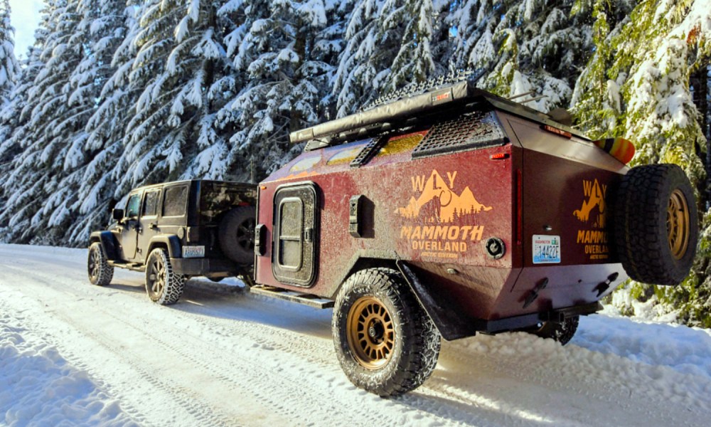 Jeep pulling a Mammoth Overland WLY Mammoth trailer up a snowy mountain road.