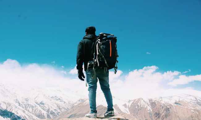 Man wearing a duffel bag as a backpack standing outside looking at mountains