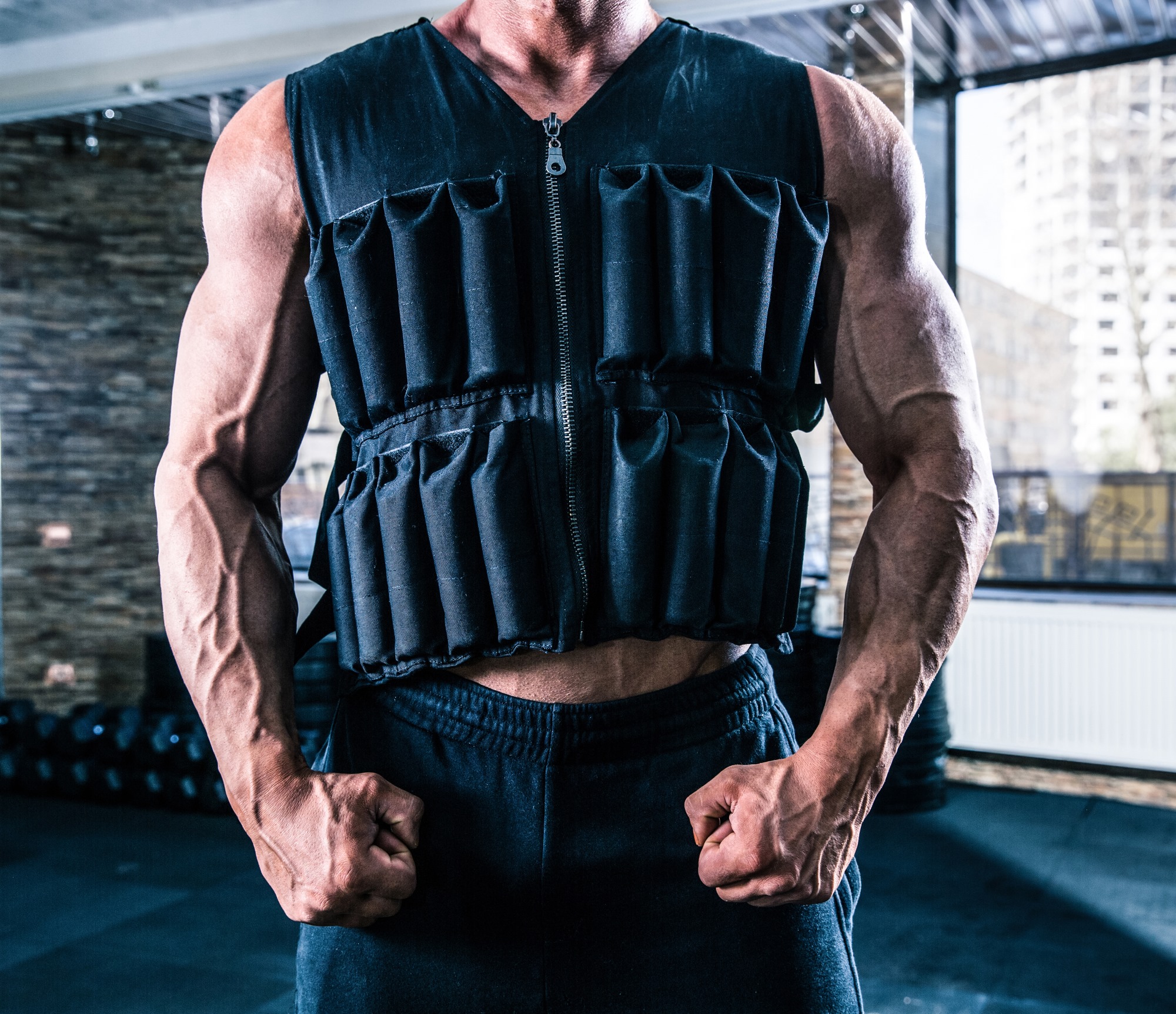 man wearing weighted vest in gym close up arms muscular muscles flex fist clench