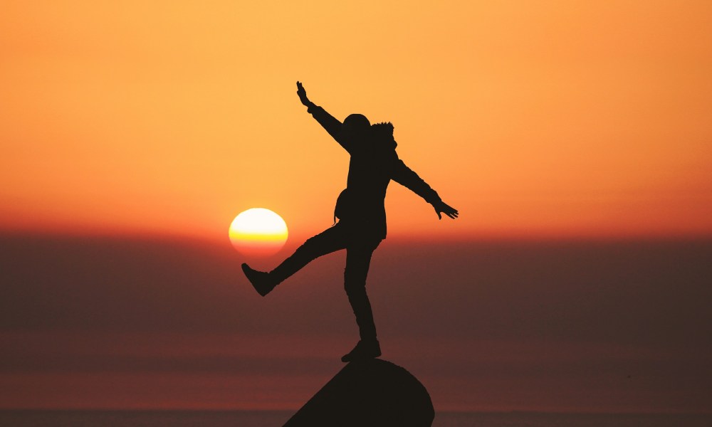 happy man silhouette outline balancing on rock sunset beach