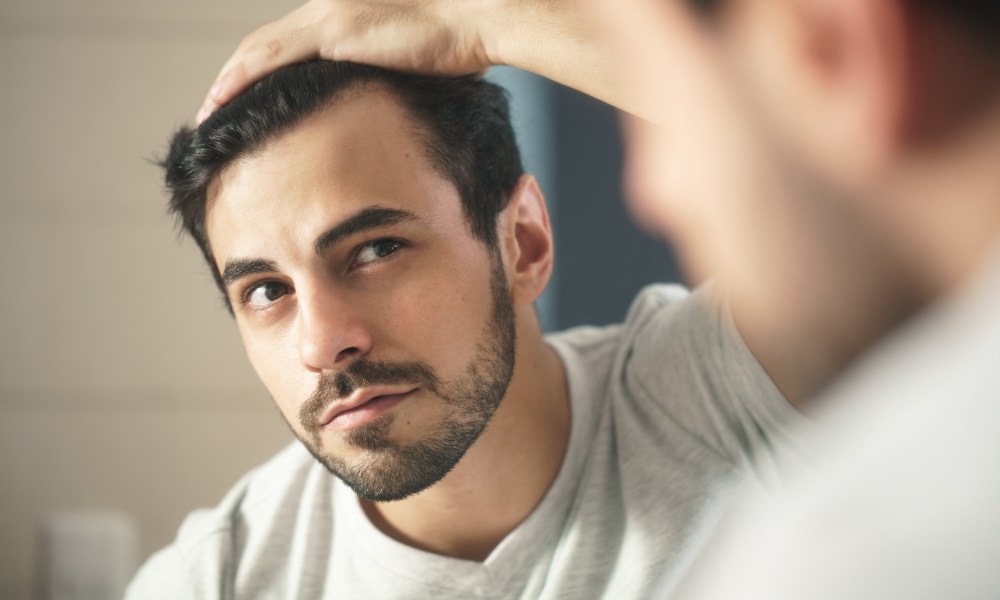 Latino person with beard grooming in bathroom at home. White metrosexual man worried for hair loss and looking at mirror his receding hairline.