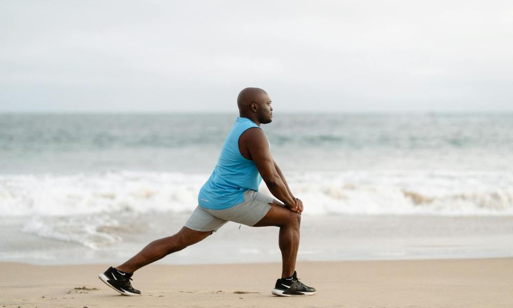 man on vacation exercising stretching legs on beach