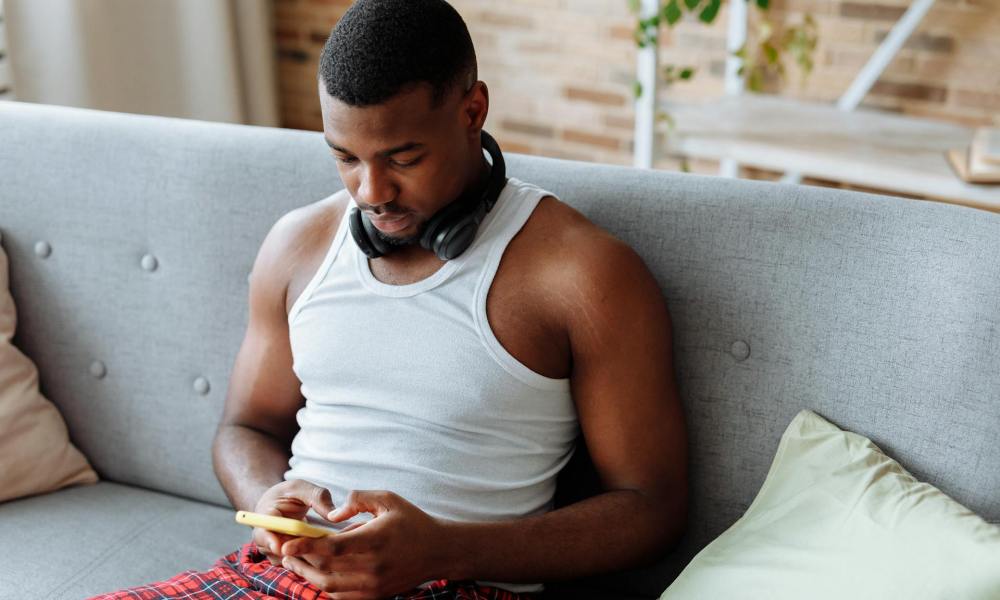 Man sitting on couch wearing headphones relaxing on phone