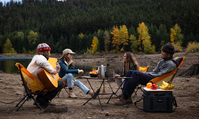 Four campers sitting near a river in Helinox Chair One (re) packable camp chairs.